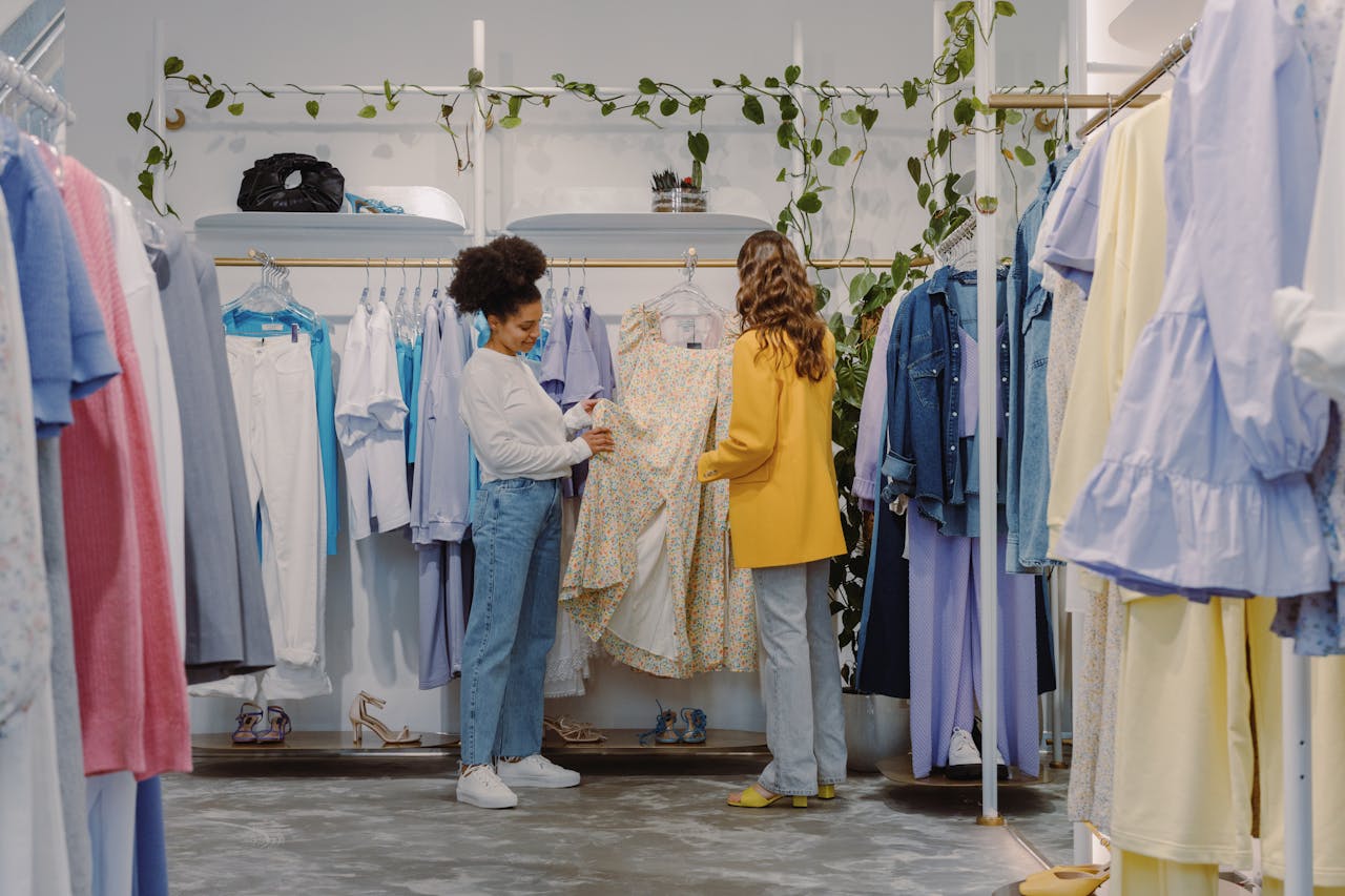 hero-img-02 Two women shopping for trendy outfits in a modern clothing boutique filled with colorful garments.