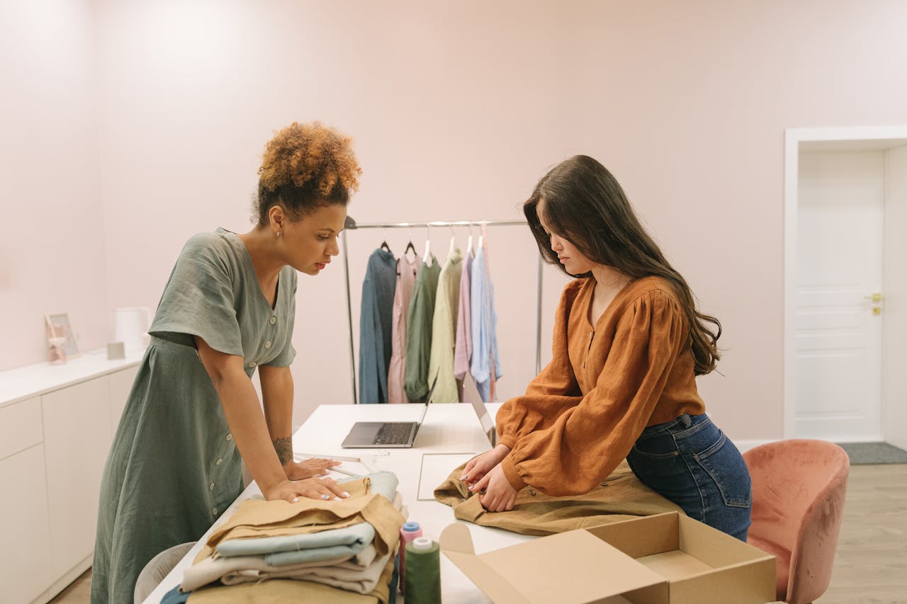 about-01 Two young women working together in a modern boutique, organizing clothes with focus and style.